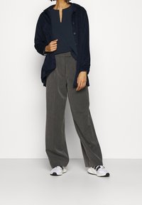 Mörkblå kordkjortsjacka över en mörk topp, ihop parat med grå vida byxor och vita sneakers med svarta detaljer.