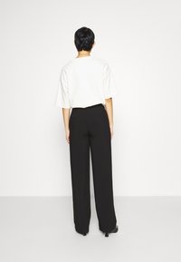 Vit överdimensionerad t-shirt med korta ärmar och svarta vida byxor. Slät tyg, minimalistisk design, enfärgade, inga synliga mönster.