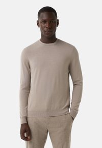 Beiger Pullover mit langen Ärmeln und rundem Ausschnitt. Glatte Strickware, gerippte Bündchen und Saum, figurbetonte Silhouette, minimalistisches Design.