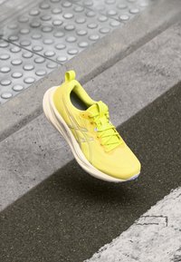 Chaussure de sport jaune avec une tige en maille respirante, des accents synthétiques, une semelle rembourrée et des détails réfléchissants. Idéale pour le sport et la course.