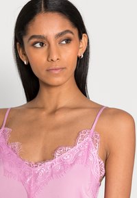 Camisola rosa com detalhes em renda ao longo do decote e das alças. Tecido suave com um acabamento delicado, apresentando um design leve e suave.