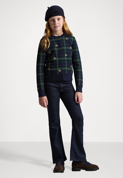 Marine rutete genser med grønne detaljer, med knappeåpning og broderte elementer, parret med mørke, vide jeans og brune sko.