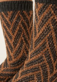 Braune und schwarze gemusterte Socken mit Chevron-Design, die metallische Fäden für Struktur enthalten, und einem gerippten Bündchen oben.