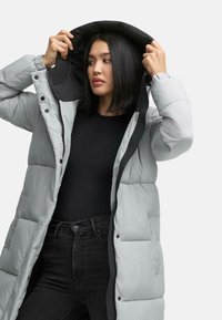 Lys grå pufferjakke med sort indvendig for og hætte, med knaplukning fortil, sidelommer og quiltet tekstur.