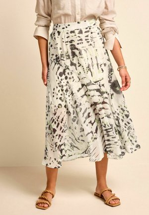 Femme portant un chemisier beige et une jupe midi fluide avec un imprimé animal abstrait noir et vert, associée à des sandales tressées couleur cognac.