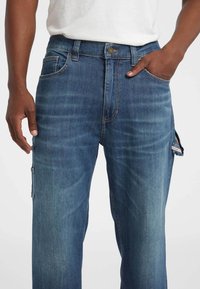 Blauwe denim cargobroek met een relaxte pasvorm, voorzien van zijzakken, een knoopsluiting en contrasterende stikseldetails.