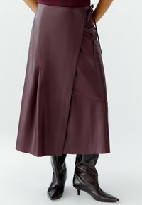 Bordeaux faux leren wikkelrok met asymmetrisch ontwerp, zijstrik en een soepele textuur. Gecombineerd met glanzende bruine kniehoge laarzen.
