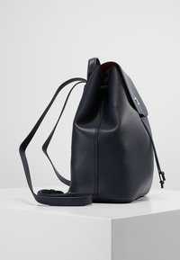 Borsa a secchiello in pelle blu navy con texture liscia, chiusura a coulisse e tracolla regolabile, caratterizzata da una forma curva elegante e hardware minimale.