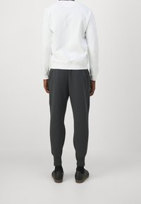 Witte sweatshirt met lange mouwen en geribbelde boorden, gecombineerd met donkere grijze tapered sweatpants. Zwarte schoenen met een gestructureerde zool.