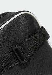 Lähikuva mustast tekstuuriga nahast kotist, millel on must reguleeritav rihm ja valged ääred kõverate servade ääres.