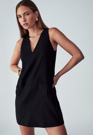 Black sleeveless dress with a v-neck, featuring two front pockets. Smooth fabric and knee-length design. Simple, modern silhouette.