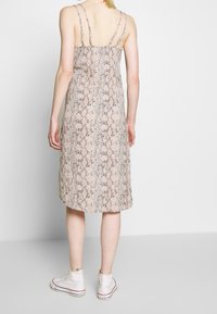 Hihaton mekko, jossa on vaaleanpunainen ja ruskea käärmeennahkakuosi. Mekossa on kaksi ohutta olkainta, ja se ulottuu polveen. Yhdistettynä valkoisiin korkean vartalon tennareihin.