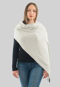 Lys grå sjal viklet om skuldrene, lavet af blødt stof med en let struktureret overflade. Har en diagonal overlapning og frynser i kanterne.
