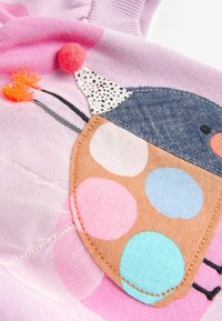 Tissu rose avec un écusson coloré de coccinelle présentant de grands pois, une tête bleue, des yeux noirs, un nez orange et des détails d'antennes orange duveteuses.
