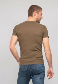 T-shirt couleur vert olive, à manches courtes, au design ajusté et à texture côtelée, porté avec un jean en denim bleu, vu de dos.