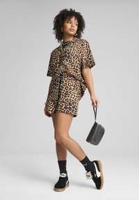 Conjunto de top y pantalones cortos de estampado de leopardo en tonos marrón y negro, combinado con zapatillas negras y un pequeño bolso negro, presenta mangas cortas y un corte relajado.