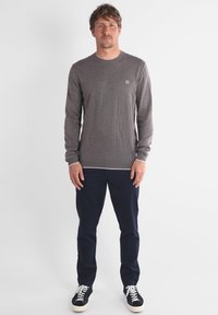 Chemise à manches longues grise avec col rond, bord blanc à l'ourlet et aux poignets, associée à un pantalon bleu foncé et des baskets noires. Design simple.