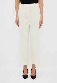 Beige op maat gemaakte broek met een rechte pijpenontwerp, voorzien van riemlussen en zakken, gecombineerd met zwarte puntige hakken.