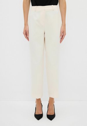 Beige tailored trousers with a straight leg design, featuring belt loops and pockets, paired with black pointed heels.