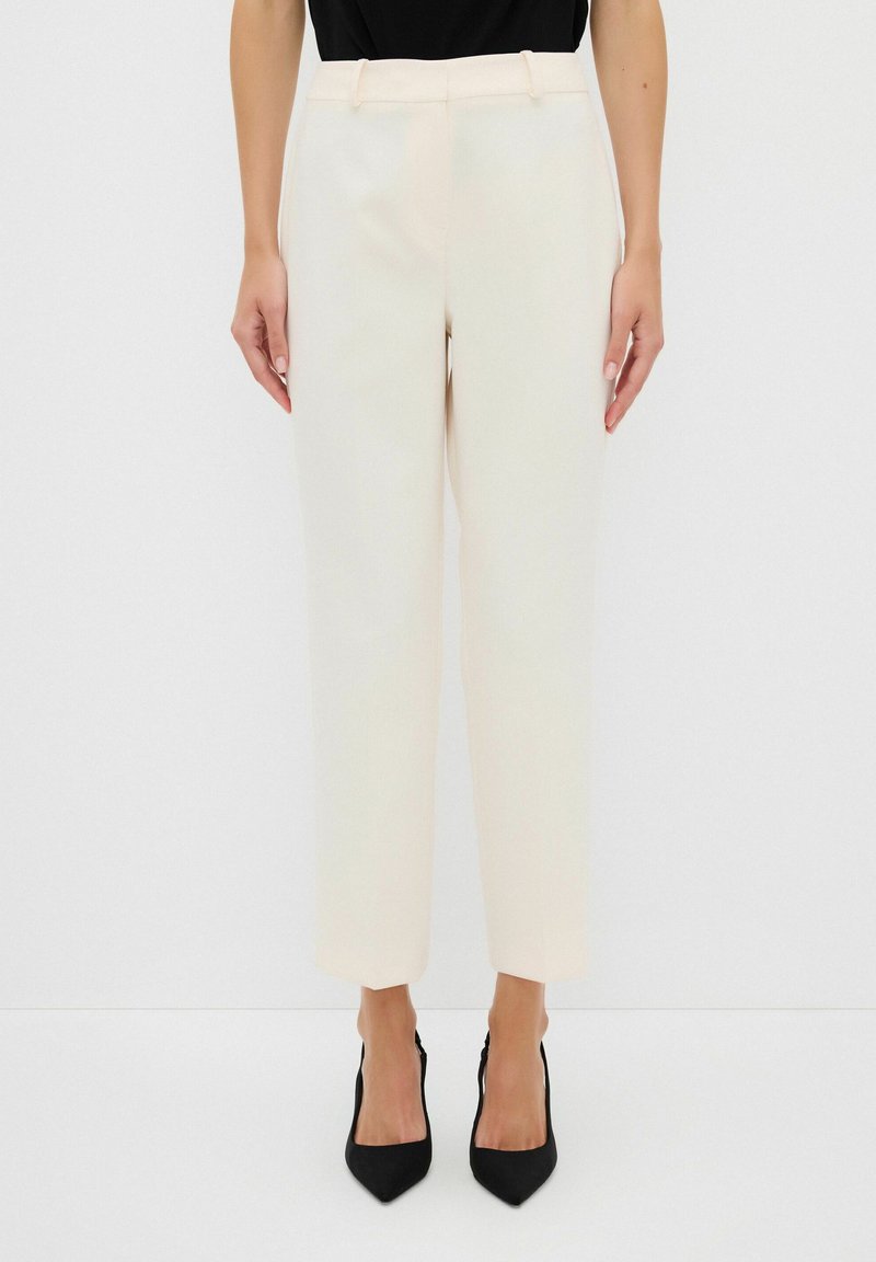 Beige op maat gemaakte broek met een rechte pijpenontwerp, voorzien van riemlussen en zakken, gecombineerd met zwarte puntige hakken.