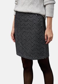 Svart och vit fiskbensmönstrad kjol i strukturerad tyg, med rak skärning och fåll, i kombination med svarta strumpbyxor.