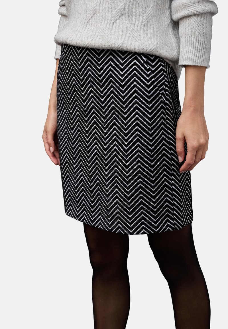 Svart och vit fiskbensmönstrad kjol i strukturerad tyg, med rak skärning och fåll, i kombination med svarta strumpbyxor.