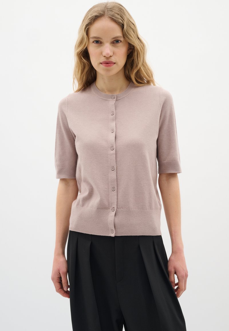 Helle rosa gestrickte Strickjacke mit kurzen Ärmeln, runder Ausschnitt und sechs Knopfverschluss. Glatte Textur, tailliert.