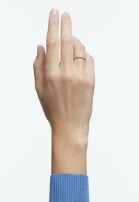 Silverring med flera klara ädelstenar, bärs på en hand mot en ljus bakgrund. Handen visar naturliga naglar; en blå ribbad tröja syns.