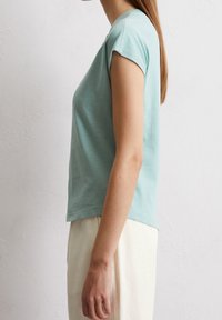 T-shirt in cotone azzurro chiaro a maniche corte con scollatura rotonda, design leggermente cropped e texture liscia, indossato con pantaloni color crema.