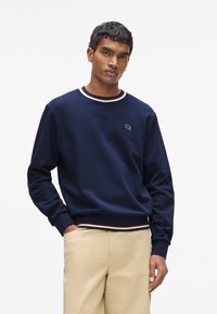 Sweat-shirt bleu marine avec col rond orné de bordures côtes rouges et blanches, manches longues et petit logo brodé sur la poitrine.