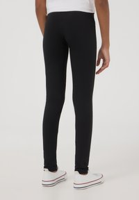 Czarne legginsy o dopasowanym kroju, wykonane z elastycznej tkaniny, z gładką fakturą i pasem w talii, zestawione z białymi trampkami.