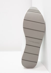 Baskets blanches avec une semelle gris texturé, présentant des rainures horizontales et un logo estampé sur le côté, mettant en avant un design moderne et durable.