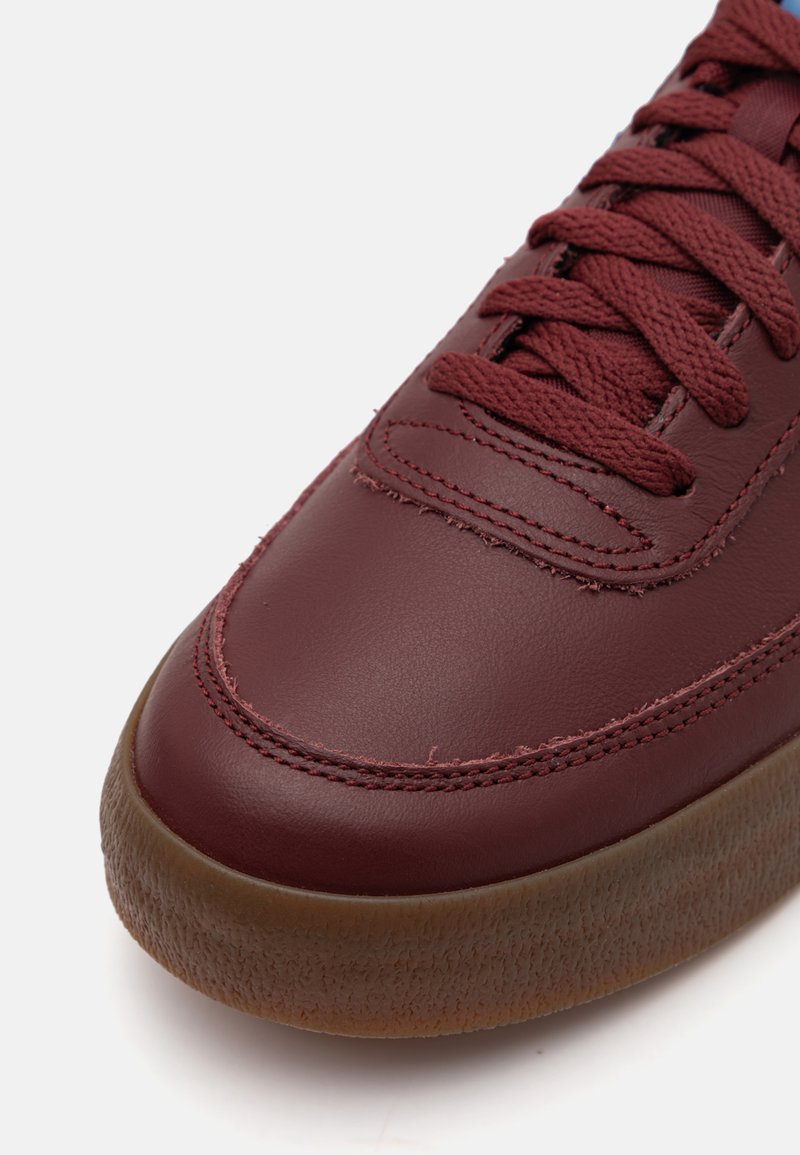Zapatillas de cuero burdeos con suela de goma texturizada, con diseño de cordones, acentos cosidos y superficie lisa.