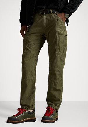 Vihreät maastohousut, joissa on useita taskuja, rento istuvuus ja kestävä kangas. Yhdistetty mustiin ja vihreisiin vaelluskengiin, joissa on punaiset nauhat.