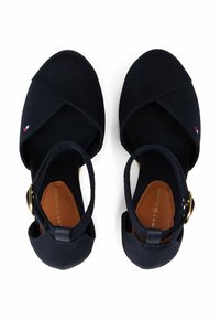 Navy canvas sandals with cross-band design, adjustable ankle strap, and brown insole featuring embossed branding. Subtle logo accent visible.