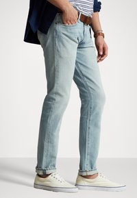 Vaaleansiniset farkut suoran leikkauksen, käännettyjen lahkeiden, viiden taskun ja ruskean nahkavyön kanssa. Yhdistettyinä valkoisiin tennareihin.