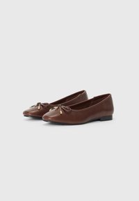 Ballerines en cuir marron avec un bout arrondi, un nœud décoratif à l'avant et de petites accents dorés sur le nœud. Design à semelle plate.