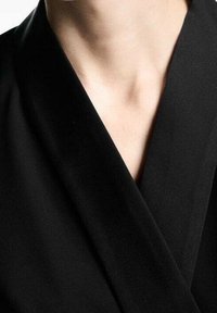 Haut cache-cœur noir avec un décolleté en V profond, en tissu lisse, présentant des bords pliés et des coutures minimales pour un design épuré.