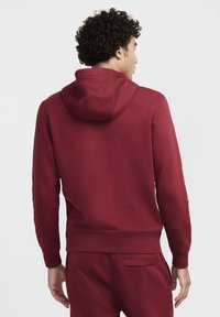 Rode hoodie met een trekkoord in de capuchon, lange mouwen en ribgebreide manchetten. De stof lijkt glad en het design bevat subtiele stikdetails.