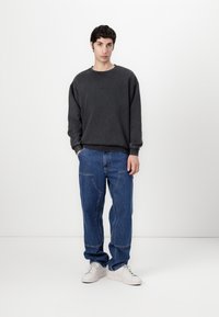 Dark gray oversized sweatshirt with a round neck, paired with loose blue jeans featuring visible seams. White sneakers complete the outfit.