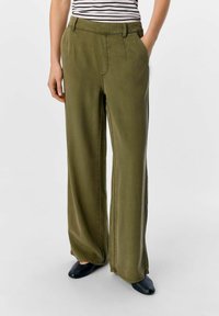 Pantalones de pierna ancha en tela verde oliva con una textura suave, cuentan con una cinturilla y bolsillos laterales. Combinados con calzado negro.