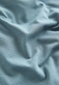 Gaiši zils, mīksts audums ar krokām, demonstrējot gludu tekstūru un maigu spīdumu. Vienmērīga krāsa bez redzamām rakstiem vai akcentiem.