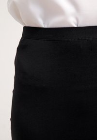 Jupe noire en tissu lisse avec une silhouette ajustée et une large ceinture. L'ourlet est net, sans attaches visibles ni ornements.