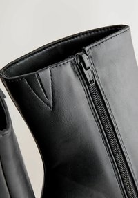 Sorte læder ankelstøvler med lynlås i siden, glat tekstur og syede detaljer på oversiden og omkring åbningen.