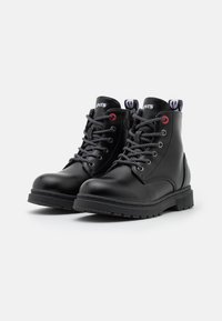 Black leather ankle boots with round toe, textured rubber sole, black lace-up closure, red eyelets, and logo detailing on the collar.