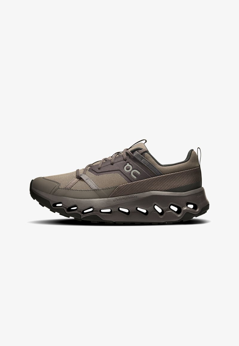 Chaussure de sport marron et grise avec un upper en mesh, un embout arrondi et une semelle découpée distinctive pour la respirabilité et le soutien.