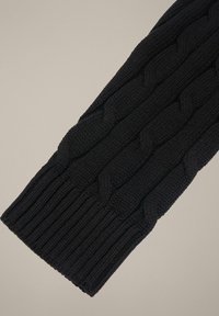 Czarny rękaw swetra z dzianiny z warkoczowym wzorem i ściągaczem. Miękka tekstura i jednolity wzór tkaniny na całej powierzchni.