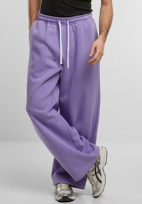 Jasnofioletowe spodnie dresowe wykonane z miękkiego materiału, z elastycznym pasem na sznurki, luźnym krojem i białymi sznurkami jako akcentem.