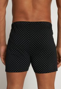 Zwarte boxershorts met witte stippen, elastische tailleband, zachte stof en een aansluitend ontwerp. Zichtbare stiksels langs de zoom.