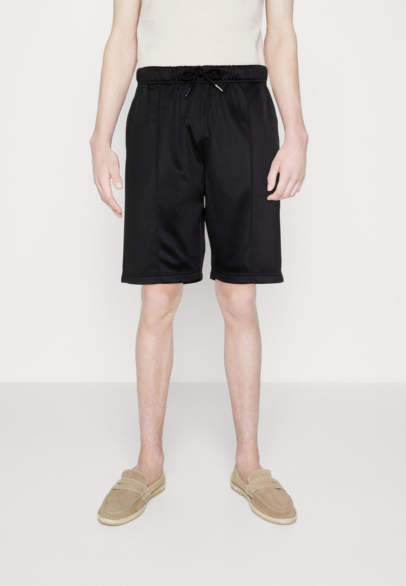Shorts de sport noirs en tissu lisse ; taille élastique avec cordon de serrage, poches latérales, longueur au genou, et coutures ajustées.